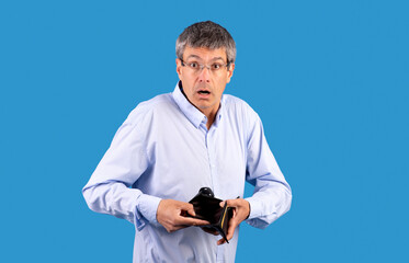 mature man bankrupt showing his empty wallet on blue backdrop