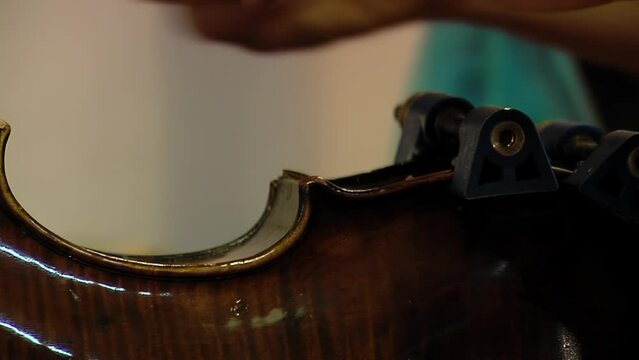 A Man Repairing a Violin in Violin Repair Workshop, Craftsman Holding Violin with Clamps during Restoration Work. Close Up.