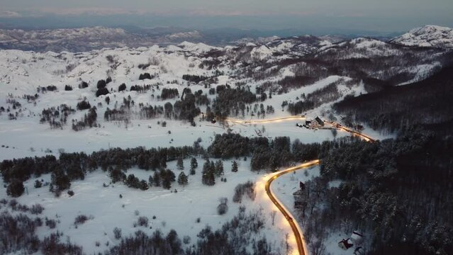 Amazing evening aerial view from drone on road between scenic mountains in winter. Top-down view of a picturesque mountain serpentine stretching into the distance. Cozy snow-covered houses