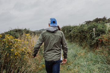A man strolls along a grassy path on the Breton coast under a gray sky.