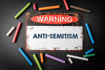 Anti-Semitism. Metal warning sign and colored pieces of chalk on a dark chalkboard background