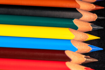 Sharp colored pencils lie in a row. Set of colored pencils on a dark surface - Powered by Adobe