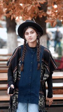 A hat-wearing and hippie-dressed beauty gracefully walks the city streets in autumn.