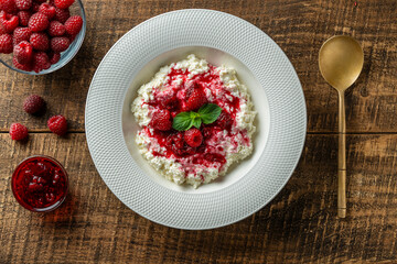 Fresh white cottage cheese with sour cream and red raspberry jam on wooden background, closeup, top view