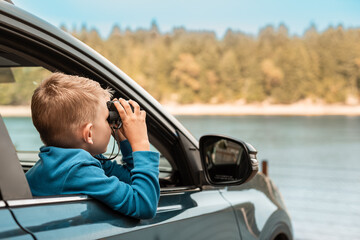 Family road trip nature adventure. child looking out of car with binoculars watching wildlife 