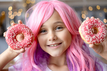 Close up Portrait of a little smiling girl with pink hair and two appetizing donuts in her hands,...