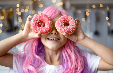 Close up Portrait of a little smiling girl with pink hair and two appetizing donuts in her hands,...