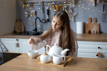 happy cute little girl in beautiful dress preparing tea, christmas morning in the kitchen....