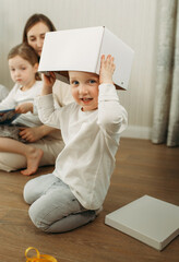 Fototapeta na wymiar A child sits on the floor with a cardboard box on his head.