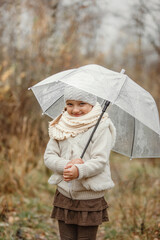 Portrait of a preschool girl standing in the park under an umbrella in the fall, smiling.