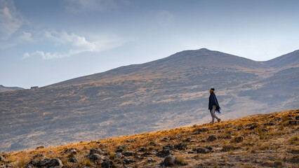 A man walking downhill wearing a black poncho in a lonely rocky and hazy landscape