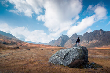 Peruvian man standing on a big rock enjoying the view of the mountains, dry season, and highlands, blue sky