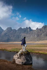 Keuken foto achterwand Alpamayo A lonely Peruvian man with black poncho and scarf standing on a large rock on the shores of a lake in the Andes mountains looking at the breadth of the landscape