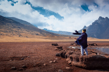 A lonely Peruvian man with a black cape and scarf standing on dried lake in the Andes mountains looking at the breadth of the landscape