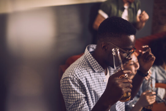Man sipping a drink thoughtfully in a busy bar