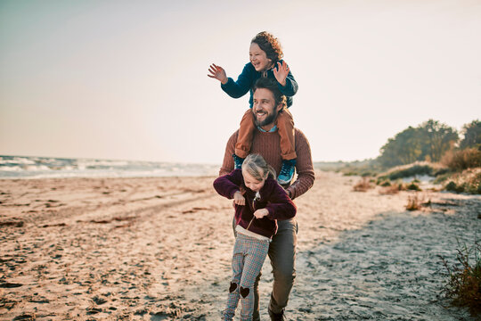 Father playing joyfully with his children on a sunlit beach