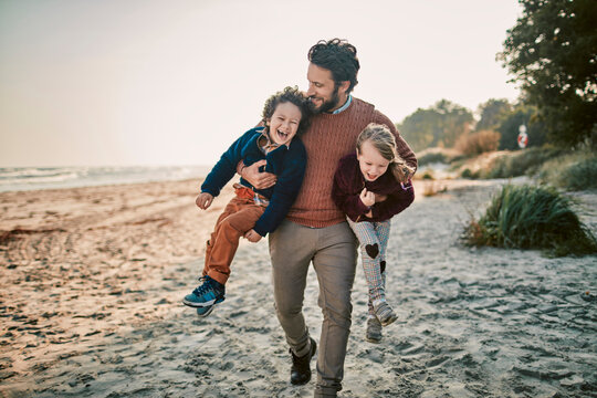 Father playing joyfully with his children on a sunlit beach