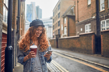 Young woman enjoying her coffee while checking her phone in a city alley