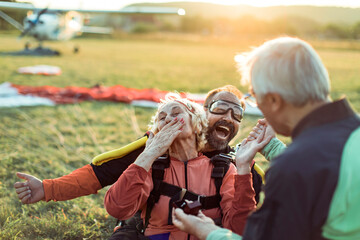 Elderly woman joyfully covers her mouth as a man proposes post-skydiving