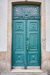 Old traditional wooden door with wrought iron door knockers on white facade in Portugal