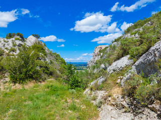 Fototapeta na wymiar Wild landscape in the Alpilles in Provence in France with a distant view of the Durance valley barely visible in the space between the two rocks, under a beautiful blue sky adorned with white clouds