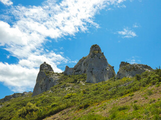 Wild landscape in the Alpilles in Provence in France with two rocky peaks.overlooking a hill covered in scrubland under blue sky dotted with white clouds