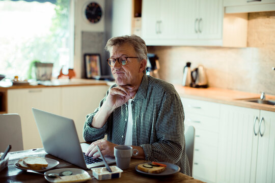 Thoughtful man works on his laptop during breakfast