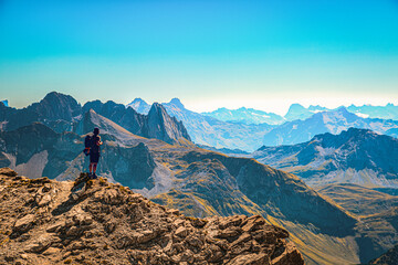 ein Wanderer steht am Gipfel den Mohnefluh im Lechquellengebirge in Österreich und schaut über...