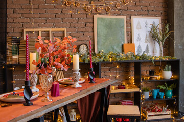 Setting the festive table. Christmas interior in red and brown colors with a brick wall. Furniture in the living room in the loft style: Christmas trees with toys