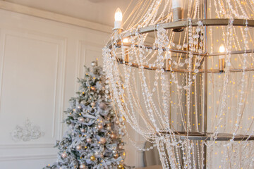 Large crystal chandelier.Christmas interior in white colors. Furniture in the living room. eleganttree with garlands.