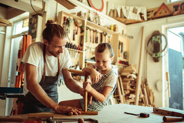 Father guiding his daughter in crafting wood in their workshop