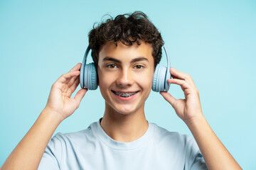 Portrait of smiling attractive boy with dental braces wearing headphones isolated on blue background