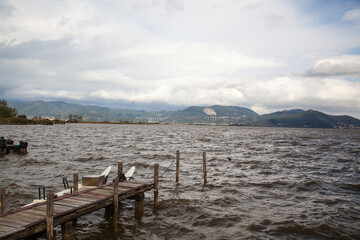 Scenery by the lake in Torre del Lago Puccini, Viareggio, Versilia, Tuscany, Italy. Wooden pier reflects in the completely calm waters projecting a reflection and pointing towards the background lands