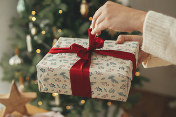 Merry Christmas and Happy holidays! Woman hands opening stylish christmas gift with red ribbon...