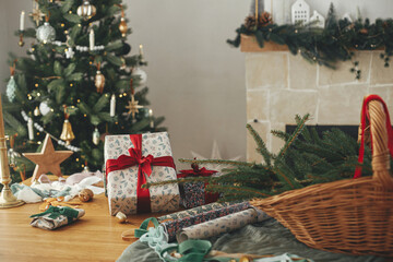 Stylish christmas gifts and festive decorations on table on background of beautiful vintage christmas tree and fireplace. Merry Christmas and Happy Holidays! Winter holidays preparation
