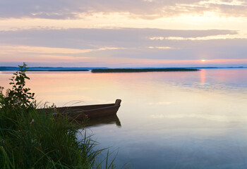 Obraz premium Sunset and old wooden fishing boat near the summer lake shore (Svityaz, Ukraine)