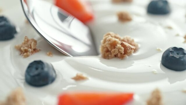Granola with Fruit Scooped with Silver Spoon from Creamy Thick Yogurt in Macro and Slow Motion