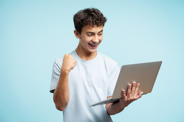 Portrait of smiling handsome teenage boy wearing dental braces holding laptop, using computer