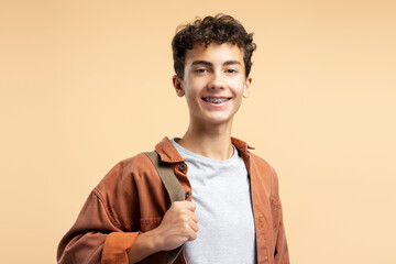 Portrait handsome teenage boy with dental braces wearing casual clothes isolated on beige background - obrazy, fototapety, plakaty
