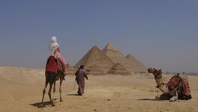 Young woman sits atop a camel in Egypt. Great Pyramids of Giza.
