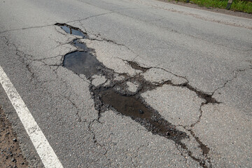 Potholes on bad asphalt road. Closeup - obrazy, fototapety, plakaty