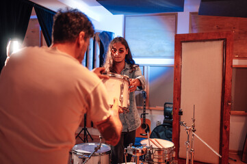Drummer setting up a tom with help of a band mate in a music studio.