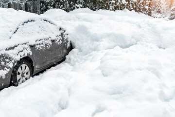 City street driveway parking lot spot with small car covered snow stuck trapped after heavy blizzard snowfall winter day by big snowy pile. Snowdrifts and freezed vehicles. Extreme weather conditions