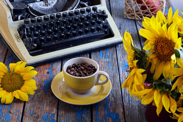 Cozy autumn tea party: a cup of tea, an old typewriter, bokeh from a bouquet of sunflowers, top view