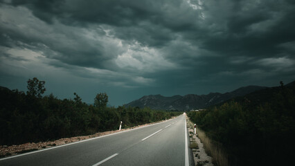 Asphalt road panorama in countryside on cloudy day. Road in forest under dramatic cloudy sky. Image of wide open prairie with a paved highway stretching out as far as the eye can see. - 671265128