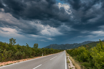 Asphalt road panorama in countryside on cloudy day. Road in forest under dramatic cloudy sky. Image of wide open prairie with a paved highway stretching out as far as the eye can see.