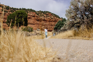 A young girl in a green sweatshirt and green pants walks among the red canyons on a sunny day....