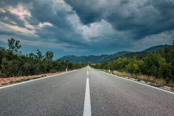 Asphalt road panorama in countryside on cloudy day. Road in forest under dramatic cloudy sky. Image of wide open prairie with a paved highway stretching out as far as the eye can see. - 671265515