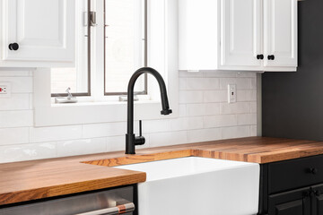 A kitchen faucet detail with white cabinets, a butcher block countertop, and a white subway tile...
