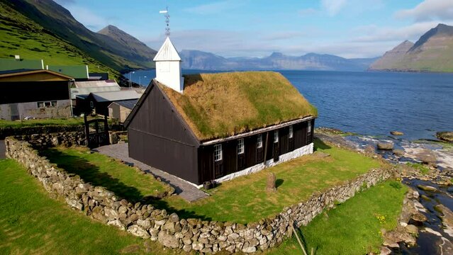 FAROE ISLANDS - JULY.16.2023 - Excellent aerial view circling a chapel with a grassy roof on the coast of Funningur in the Faroe Islands.